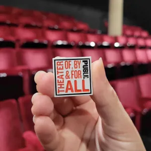 Hand showcasing 1" Theater Of By & For All Enamel Pin.